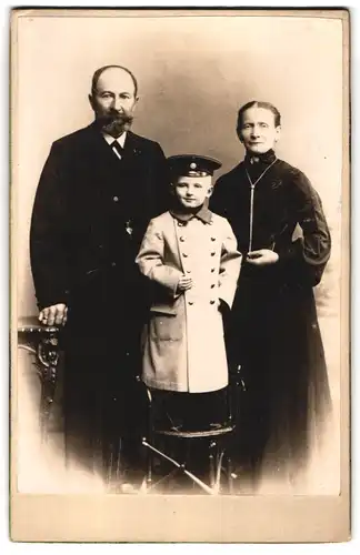 Fotografie unbekannter Fotograf und Ort, Kleiner Bursche in Uniform mit Schirmmütze mit den Eltern