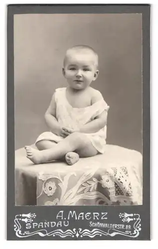 Fotografie A. Maerz, Spandau, Schönwalderstrasse 89, Baby in Strampelkleidchen, auf einem Tisch sitzend