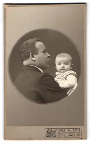 Fotografie Wilh. Klemm, Schwäbisch Hall, Vater im Nadelstreifenanzug mit seinerm Kind im Arm, schaut über die Schulter