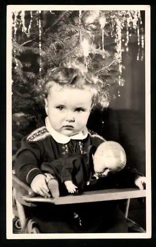Fotografie Weihnachten, Baby mit Puppe vor dem Weihnachtsbaum sitzend
