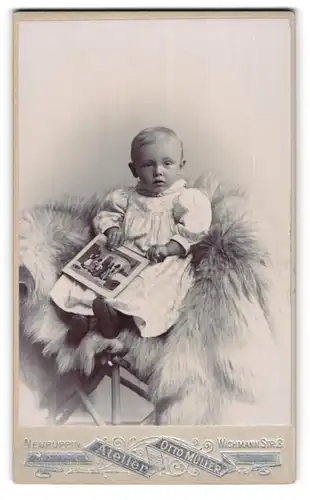 Fotografie Otto Müller, Neuruppin, Wichmannstr. 8, Kleines Kind im Kleid mit Bilderbuch sitzt auf Fell