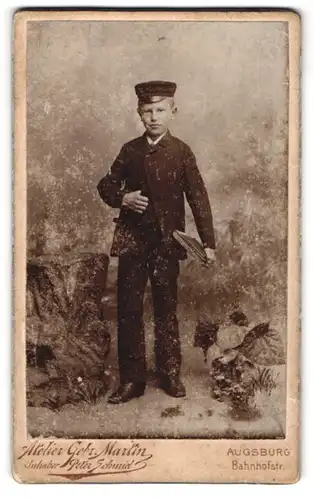 Fotografie Peter Schmid, Augsburg, Bahnhof-Str., Halbwüchsiger Knabe im Anzug mit Schirmmütze und Büchern