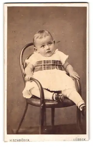 Fotografie H. Schröder, Lübeck, Beckergrube 150, Kleiner Junge im Kleid sitzt auf einem Stuhl