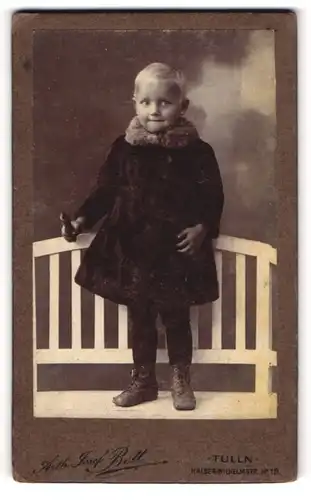 Fotografie Anth. Josef Bett, Tulln, Kaiser-Wilhelm-Str. 19, Portrait blonder frecher Bube im Mantel mit Fellkragen