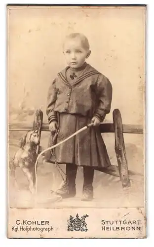 Fotografie C. Kohler, Stuttgart, Schellingstr. 13, Kleiner Junge im Kleid mit Spielzeugpferd