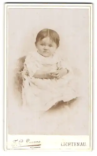 Fotografie F. C. Lauppe, Lichtenau, Süsses Kleinkind im Kleid sitzt auf Fell