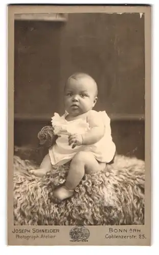 Fotografie Joseph Schnieder, Bonn a. Rh., Coblenzerstr. 25, Süsses Kleinkind im Hemd sitzt auf Fell