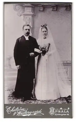 Fotografie Ekström & Westergaard, Upsala, Pfarrer im Talar mit Umhang nebst seiner Braut im Hochzeitskleid