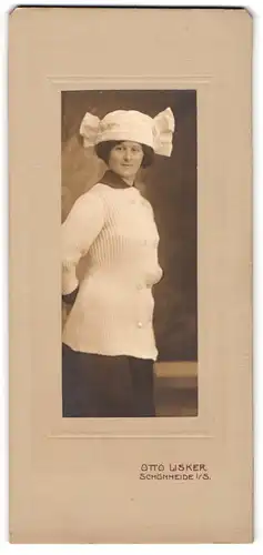 Fotografie Otto Lisker, Schönheide i. S., Portrait Frau posiert im gestrickten Wollpullover mit Mütze samt Schleife