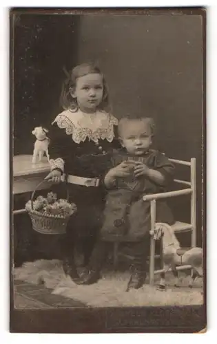 Fotografie Wilhelm Klopp & Co., Braunschweig, Portrait zwei junge Mädchen im Samtkleid mit Plüschhund und Spielzeugpferd