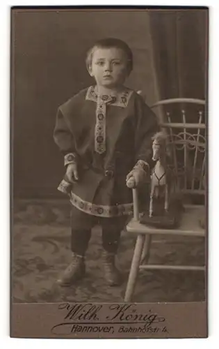 Fotografie Wilh. König, Hannover, Bahnhofstr. 4, junger Knabe im Kleid mit seinem Spielzeugpferd