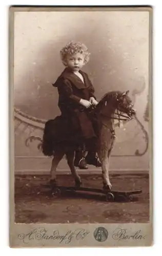Fotografie A. Jandorf & Co., Berlin, Brunnen-Str. 19, Portrait Kleinkind im Kleid mit Locken auf seinem Schaukelpferd