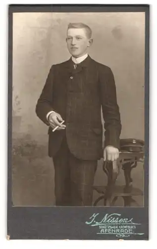 Fotografie J. Nissen, Apenrade, Portrait junger Däne im karierten Anzug posiert rauchend im Atelier