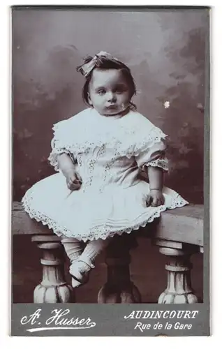 Fotografie A. Husser, Audincourt / Doubs, Rue de la Gare, Mädchen im weissen Kleidchen auf Brüstung sitzend