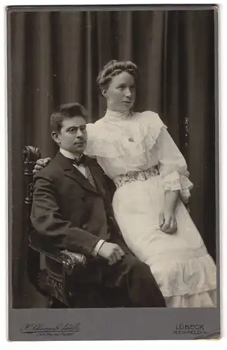Fotografie H. Schweigerle, Lübeck, Breitestrasse 31, Junges Paar in eleganter Kleidung - Sie sitzt auf seinem Schoss