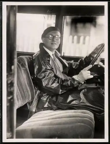 Fotografie Auto-Fahrer mit regenmantel & Hornbrille hinterm Steuer sitzend