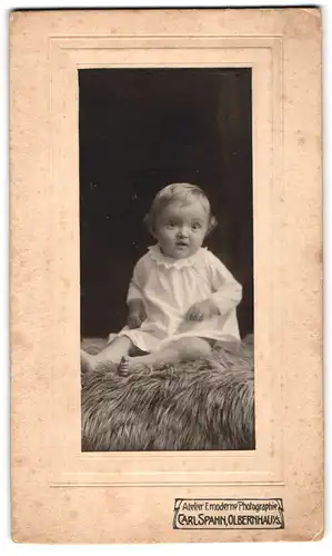 Fotografie Carl Spahn, Olbernhau i /S., Süsses Kleinkind im Hemd sitzt auf Fell