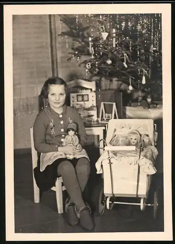 Fotografie Weihnachten, glückliches Mädchen mit Puppe, Puppenwagen & Puppenstube am Weihanchtsbaum