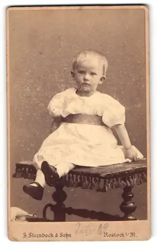 Fotografie S. Steenbock & Sohn, Rostock i /M., Kossfelder-Str. 7, Kind im weissen Kleid sitzt auf einem Tisch