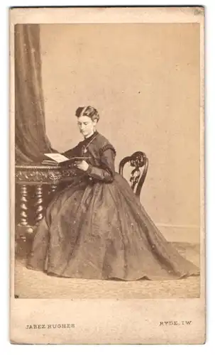 Fotografie Jabez Hughes, Ryde, Portrait junge Frau im Reifrockkleid sitzt lesend im Atelier