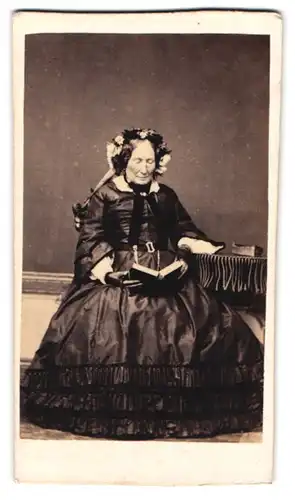 Fotografie Gilbert Aine, Ort unbekannt, Portrait ältere Dame im seidenen Biedermeierkleid lesend im Atelier