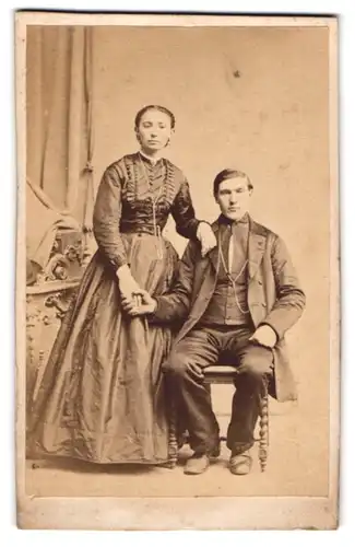 Fotografie unbekannter Fotograf und Ort, Paar im seidenen Biedermeierkleid und Anzug halten Händchen im Atelier