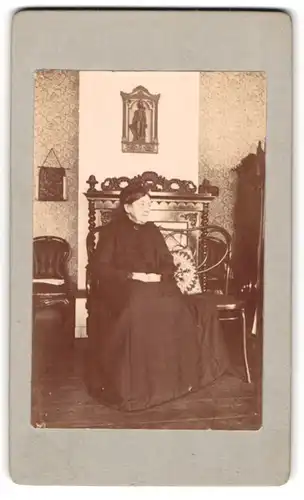 Fotografie unbekannter Fotograf und Ort, ältere Dame im heimischen Wohnzimmer mit Blümchentapete vor dem Kamin