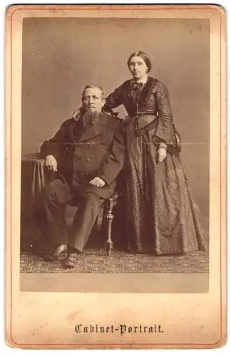 Fotografie unbekannter Fotograf und Ort, Portrait Eheleute im gepunktetem Biedermeierkleid und Anzug im Atelier