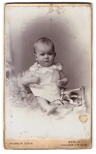 Fotografie Atelier Stein, Berlin, Chausseestr. 65-66, Süsses Kleinkind im Hemd mit Spielzeugpferd sitzt auf Fell