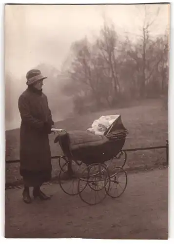 Fotografie unbekannter Fotograf und Ort, junge Mutter mit Baby im Kinderwagen beim Spaziergang