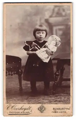 Fotografie C. Overheydt, Ruhrort a. Rh., Portrait süsses Mädchen im Samtkleid mit ihrer Puppe im Arm