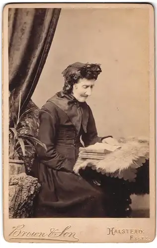 Fotografie Brown & Son, Halstead / Essex, Portrait ältere Dame im Biedermeierkleid mit Haube liest eine Buch