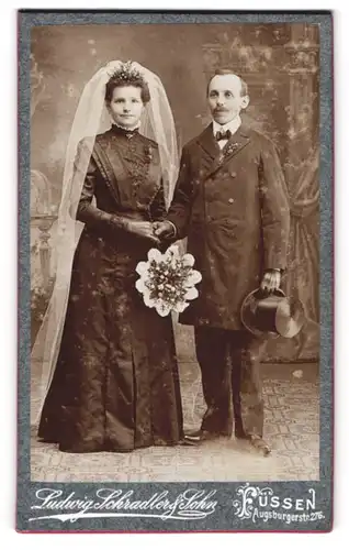 Fotografie Ludwig Schradler & Sohn, Füssen, Augsburgerstr. 276, Eheleute um schwarzen Hochzeitskleid und Anzug, Zylinder