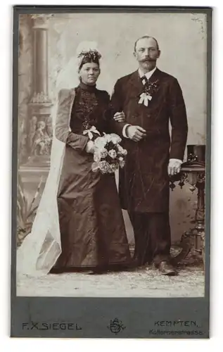 Fotografie F. X. Seigel, Kempten, Kotternerstr., Brautpaar im schwarzen Hochzeitskleid und Anzug mit Schleifen