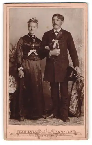 Fotografie F. X. Siegel, Kempten, Kotternerstr., Brautpaar im schwarzen Hochzeitskleid und Anzug mit Schleifen