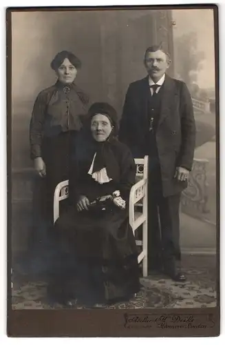 Fotografie H. Deike, Hannover-Linden, Deisterstr. 7, Ältere Dame im Kleid mit Haube sitzt vor Mann und Frau