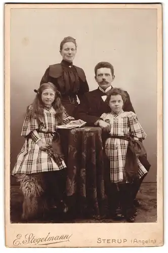 Fotografie E. Stegelmann, Sterup /Angeln, Bürgerliches Paar mit zwei Töchtern am Tisch