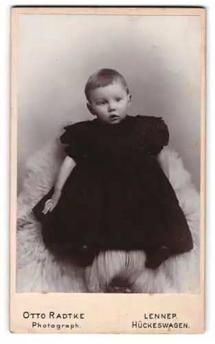 Fotografie Otto Radtke, Lennep, Süsses Kleinkind im Kleid sitzt auf Fell