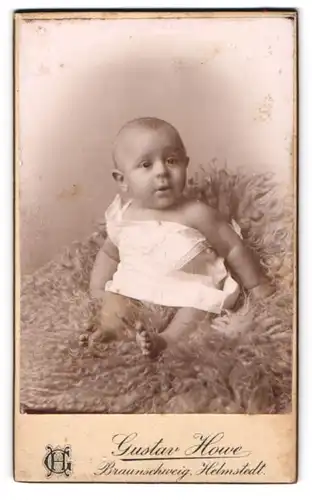 Fotografie G. Howe, Braunschweig, Steinweg 43, Süsses Kleinkind im weissen Hemd sitzt auf Fell