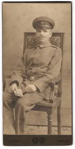 Fotografie J. Fuchs, Berlin, Rosenthalerstrasse 72a, Soldat in Uniform unbequem auf einem Holzstuhl sitzend
