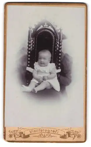 Fotografie unbekannter Fotograf und Ort, Baby im kurzen Kleidchen, an einem Stuhl festgebunden
