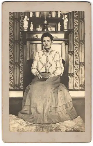 Fotografie unbekannter Fotograf und Ort, Frau im Biedermeierkleid vor e. zeitgenössischen Schrank mit Porzellanfiguren