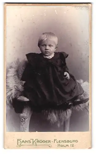Fotografie Hans Kröger, Flensburg, Holm 12, Portrait blondes Kind im schwarzen Kleid auf Fell sitzend