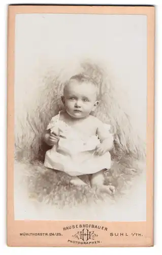 Fotografie Hause & Hofbauer, Suhl i. Th., Mühlthorstr. 124 /125, Portrait süsses Baby im weissen Hemdchen auf Fell sitzend