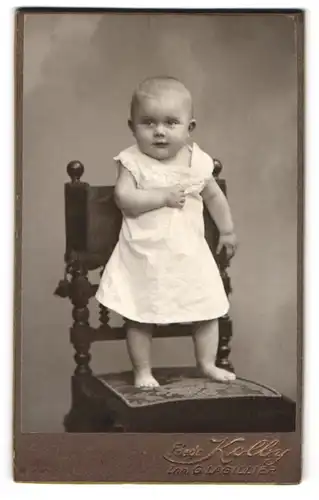 Fotografie Friedr. Kolby, Plauen i /V., Rädelstr. 1, Süsses Kleinkind im weissen Kleid steht auf Stuhl