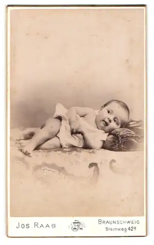 Fotografie Jos. Raab, Braunschweig, Steinweg 42, Auf der Seite liegendes Baby im kurzen Kleidchen