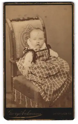 Fotografie George Aulmann, Offenbach /M., Hospitalstrasse 16, Baby in kariertem Kleidchen auf einem Sitzmöbel