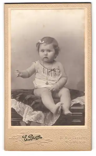 Fotografie E. Bron, Lyon, Rue Grenette 31, Kleinkind mit Schleifchen im Haar auf einem Kissen