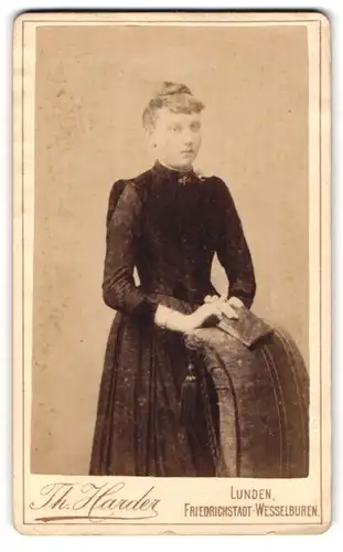 Fotografie Th. Harder, Lunden, Junge Dame im schwarzen Kleid an einem Sessel stehend