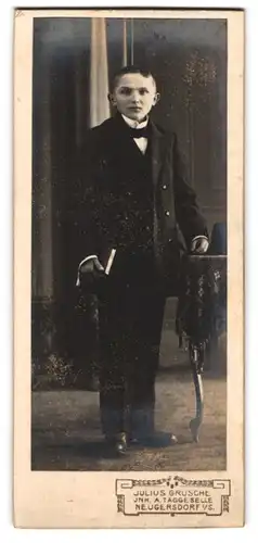 Fotografie Julius Grusche, Neugersdorf i. S., Portrait junger Knabe im schwarzen Anzug mit Fliege zur Konfirmation